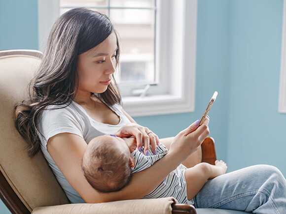 Une maman assise avec son bébé dans les bras regarde son téléphone.