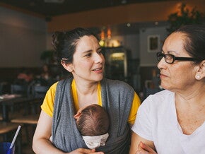 Mutter mit Baby in der Trage unterhält sich mit einer älteren Frau