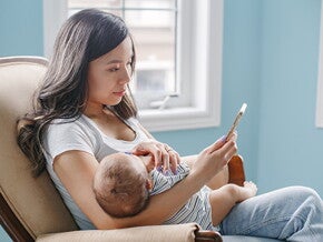 Mutter mit Baby im Arm, die auf ihr Telefon schaut