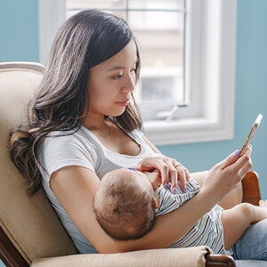 Mutter mit Baby im Arm, die auf ihr Telefon schaut