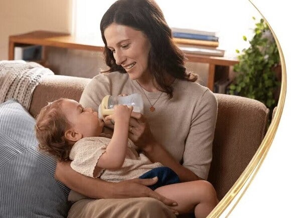 Frau, die lächelt, während sie ihrem Kleinkind auf einer Couch die Flasche gibt